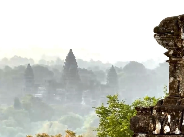 សម្រស់ដ៏ល្អឯក នៃប្រាង្គប្រាសាទអង្គរវត្ត ពីជ្រុងម្ខាងនៃភ្នំបាខែង អមដោយដើមឈើ ប្រៀបបានជាឋានសួគ៍​ក្រោមមេឃ